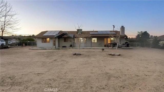 back of house at dusk with a patio, solar panels, and fence