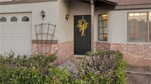 doorway to property featuring brick siding, roof with shingles, an attached garage, and stucco siding