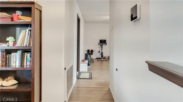 hall featuring wood finished floors, visible vents, and baseboards