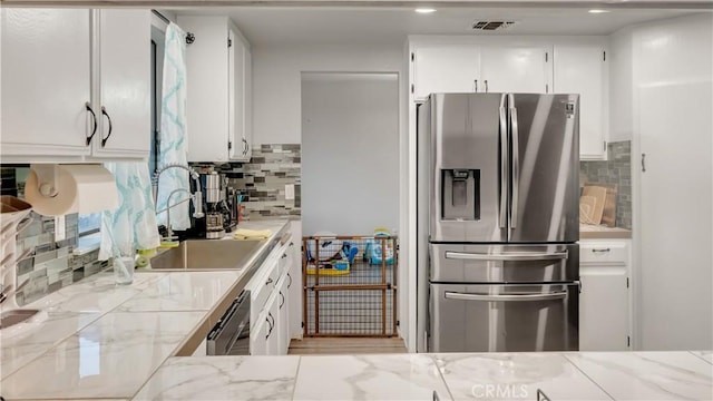 kitchen with stainless steel refrigerator with ice dispenser, visible vents, decorative backsplash, white cabinetry, and a sink