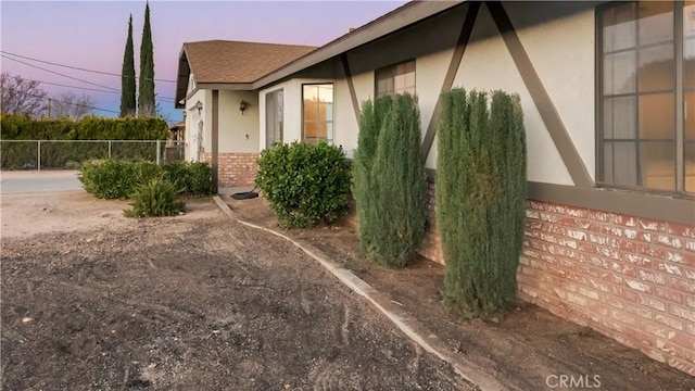 view of side of property with stucco siding, roof with shingles, fence, and brick siding