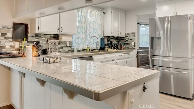 kitchen with a peninsula, a sink, white cabinets, and stainless steel fridge with ice dispenser