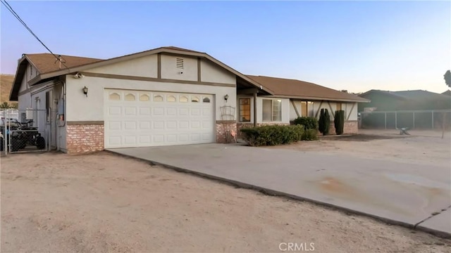 single story home with driveway, brick siding, an attached garage, fence, and stucco siding