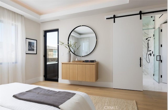 bedroom featuring baseboards, light wood-style flooring, ensuite bath, and a barn door