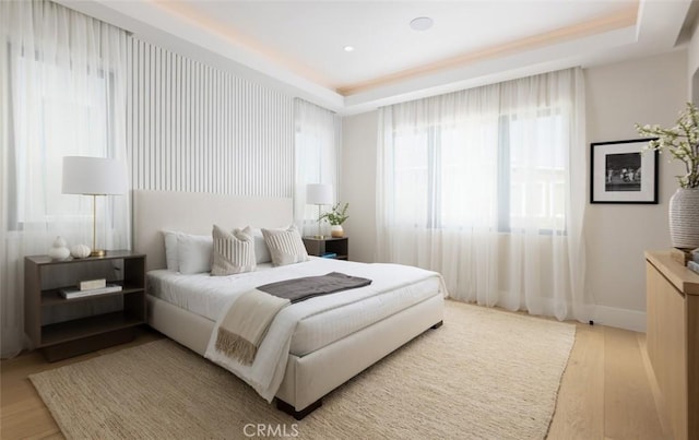 bedroom featuring a tray ceiling, baseboards, and wood finished floors