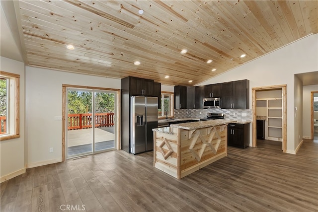 kitchen featuring a kitchen island, a sink, vaulted ceiling, stainless steel appliances, and backsplash