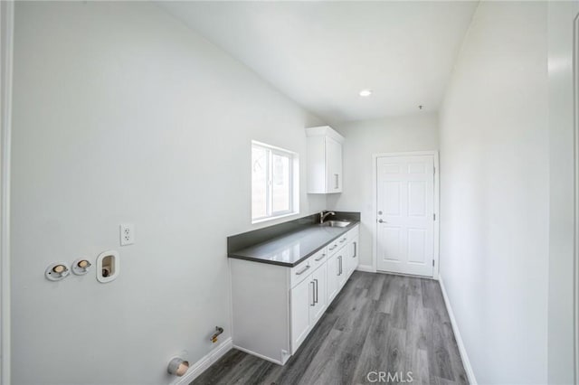 laundry room with cabinet space, baseboards, a sink, and wood finished floors