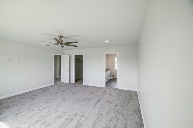 unfurnished bedroom featuring baseboards, ceiling fan, ensuite bathroom, a walk in closet, and carpet floors