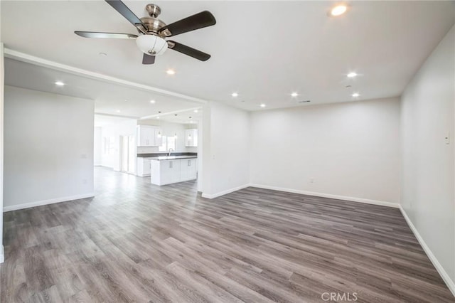 unfurnished living room with recessed lighting, a sink, baseboards, and wood finished floors