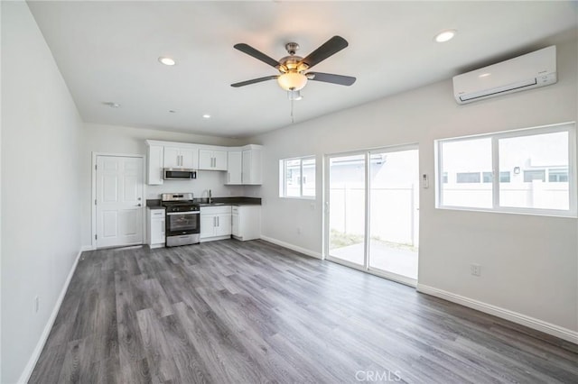 kitchen with appliances with stainless steel finishes, a wall unit AC, wood finished floors, and baseboards