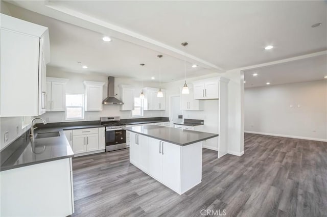 kitchen featuring dark countertops, wall chimney exhaust hood, stainless steel range with gas stovetop, wood finished floors, and a sink