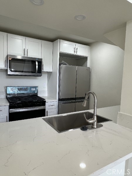 kitchen with range with gas stovetop, stainless steel microwave, freestanding refrigerator, white cabinetry, and a sink