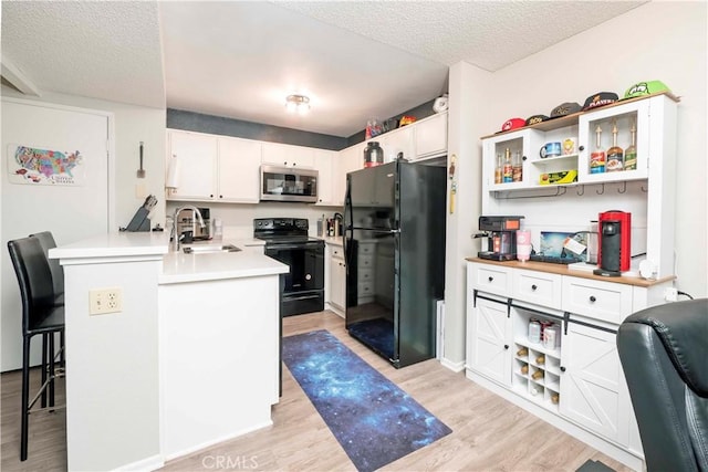 kitchen with a peninsula, a sink, light countertops, light wood-type flooring, and black appliances