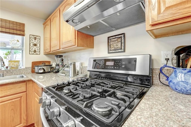 kitchen featuring light countertops, gas stove, light brown cabinets, a sink, and under cabinet range hood