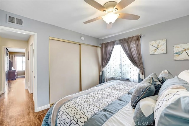 bedroom with baseboards, visible vents, ceiling fan, wood finished floors, and a closet