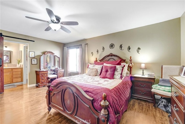 bedroom featuring a barn door, baseboards, connected bathroom, ceiling fan, and wood finished floors