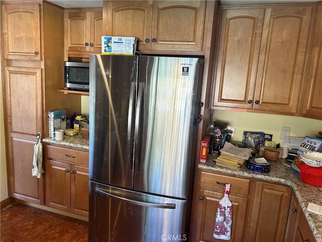 kitchen with stainless steel appliances, light stone counters, and brown cabinetry