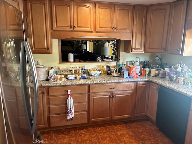 kitchen featuring brown cabinetry, freestanding refrigerator, and light stone countertops