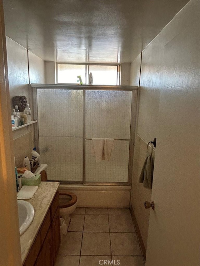 bathroom featuring toilet, tile patterned flooring, combined bath / shower with glass door, and vanity