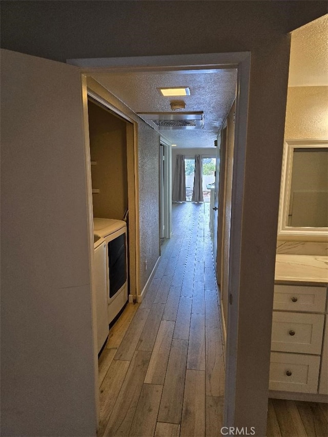 corridor with a textured ceiling, wood finished floors, and washing machine and clothes dryer