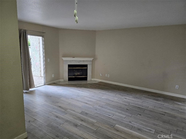 unfurnished living room with baseboards, wood finished floors, and a high end fireplace