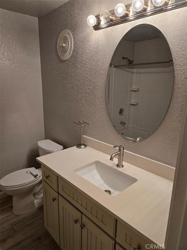 full bath featuring walk in shower, toilet, a textured wall, wood finished floors, and vanity