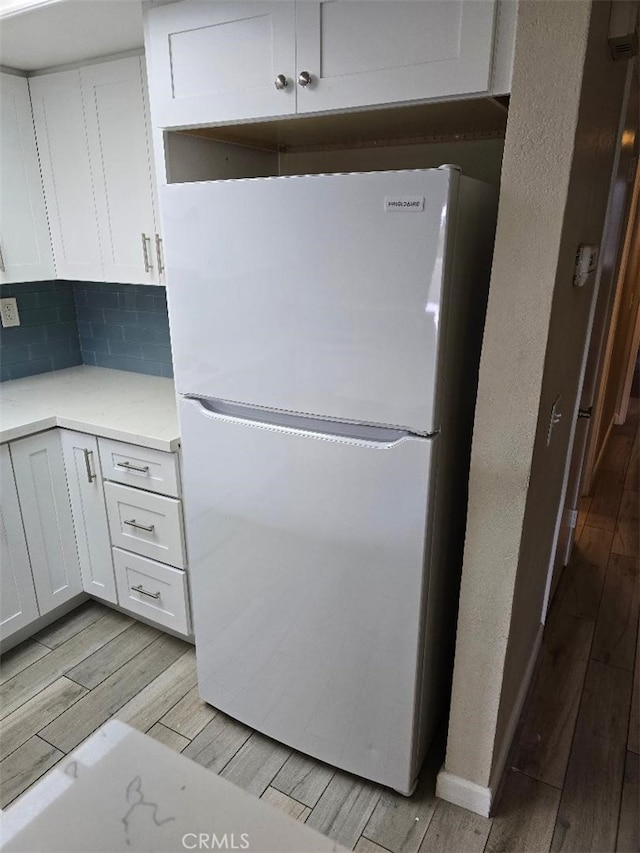 kitchen featuring decorative backsplash, white cabinets, freestanding refrigerator, and wood tiled floor