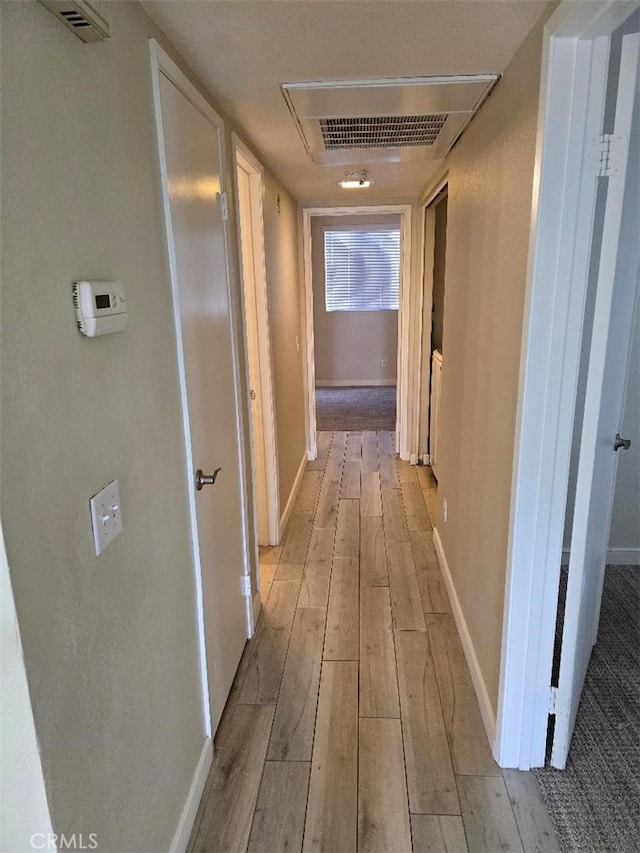 corridor featuring light wood-style flooring, baseboards, and visible vents