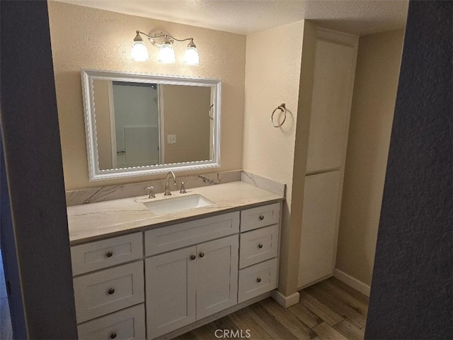 bathroom featuring baseboards, vanity, a textured wall, and wood finished floors