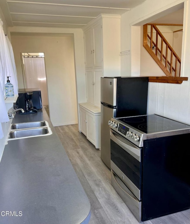 kitchen featuring a sink, white cabinets, stainless steel range with electric cooktop, light countertops, and light wood finished floors