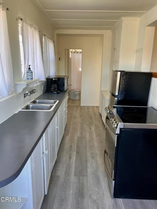 kitchen with stainless steel appliances, dark countertops, white cabinetry, a sink, and light wood-type flooring