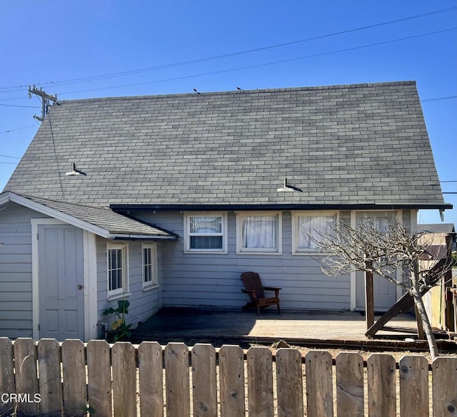 rear view of house featuring roof with shingles, fence, and a deck