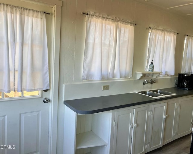 kitchen with dark countertops, white cabinets, a sink, and open shelves