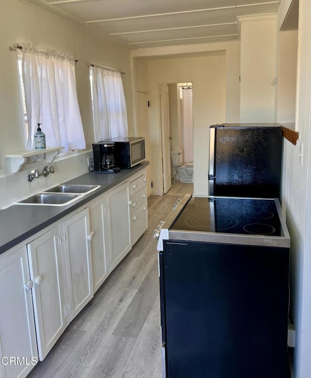 kitchen with light wood-style floors, freestanding refrigerator, white cabinetry, a sink, and range with electric cooktop