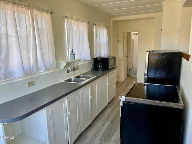 kitchen with white cabinets, electric range oven, light wood-style flooring, freestanding refrigerator, and a sink