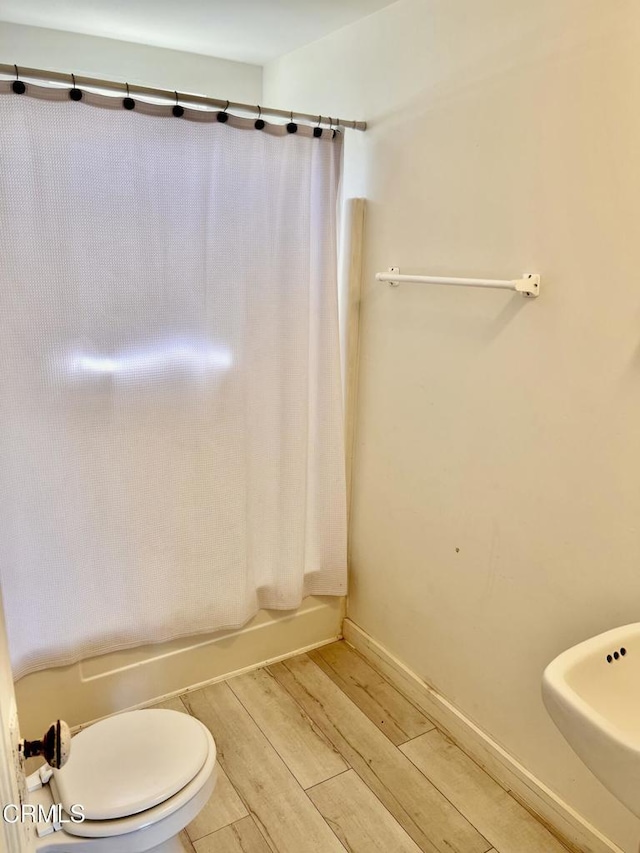 full bath with baseboards, toilet, wood finished floors, shower / bathtub combination with curtain, and a sink