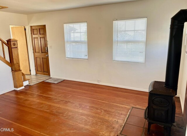 unfurnished living room with baseboards, wood finished floors, a wood stove, and stairway