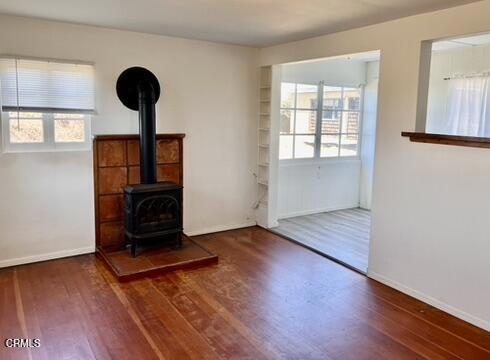 unfurnished living room with baseboards, wood finished floors, and a wood stove