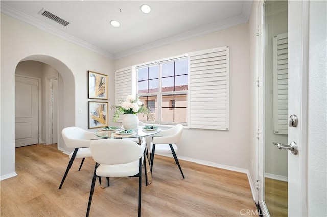 dining area with arched walkways, light wood finished floors, visible vents, ornamental molding, and baseboards