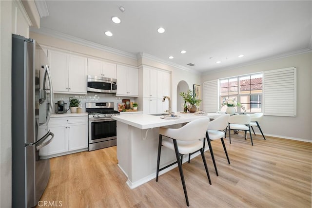 kitchen with ornamental molding, stainless steel appliances, a kitchen bar, white cabinetry, and a sink