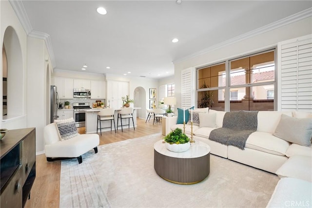 living area with light wood-style floors, arched walkways, crown molding, and recessed lighting