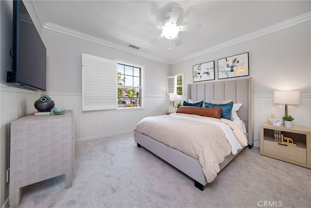 bedroom featuring a wainscoted wall, visible vents, ornamental molding, carpet flooring, and ceiling fan