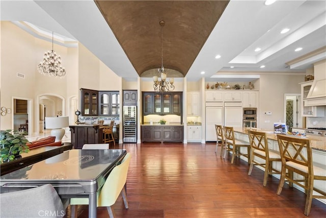 dining space with arched walkways, dark wood finished floors, a notable chandelier, recessed lighting, and vaulted ceiling