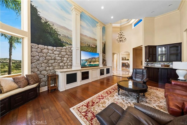 living area with arched walkways, a towering ceiling, hardwood / wood-style flooring, and crown molding