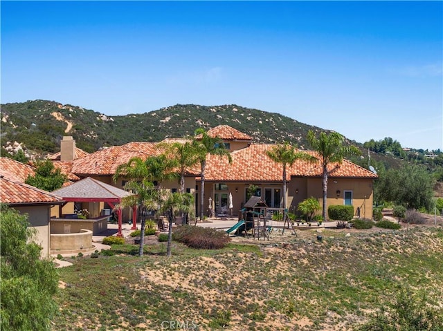 back of house featuring a playground, stucco siding, a gazebo, a mountain view, and a tiled roof