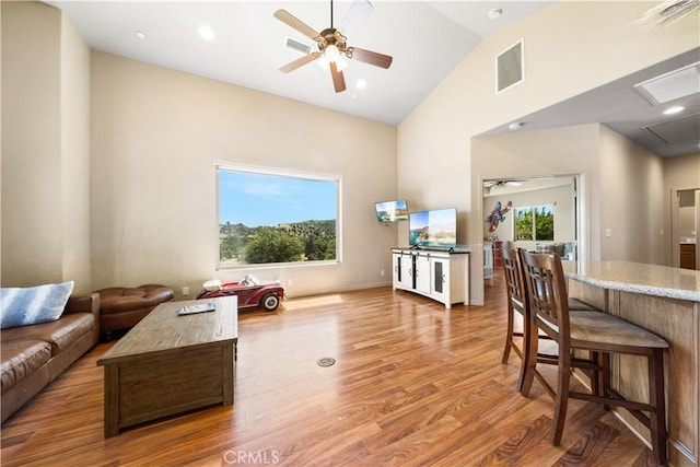 living area with high vaulted ceiling, a wealth of natural light, visible vents, and wood finished floors