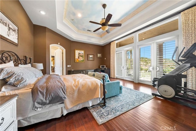 bedroom with arched walkways, wood finished floors, access to exterior, ornamental molding, and a tray ceiling