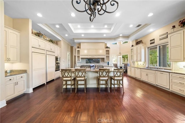 kitchen featuring stainless steel appliances, backsplash, open shelves, a tray ceiling, and a kitchen bar