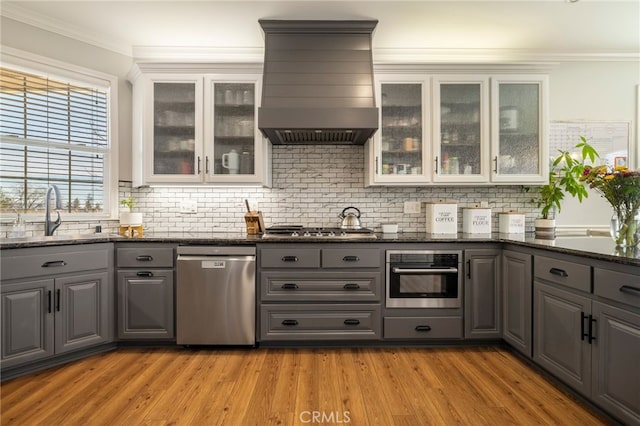 kitchen with a sink, stainless steel appliances, wall chimney range hood, and gray cabinets