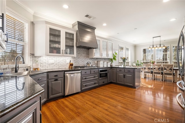 kitchen featuring visible vents, custom range hood, appliances with stainless steel finishes, a peninsula, and a sink